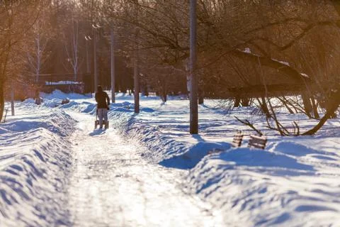 A man with a stroller strolls along the snow-covered park avenue lit by the r Stock Photos