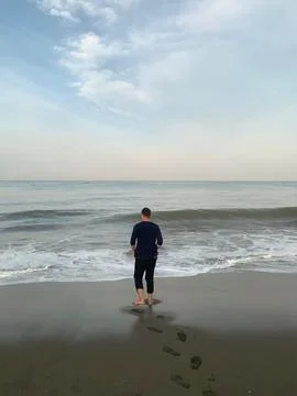 Man Strolling on Sandy Beach by the Ocean During Peaceful Morning Stock Photos