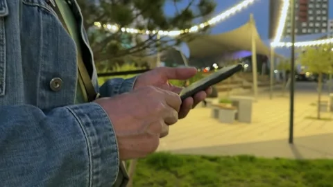 Man strolls through a city park lit with string lights in the evening, hold.. Stock Footage 339854781