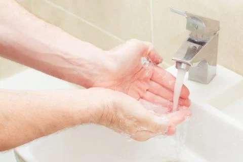 Man strong hands wash with soap in a beautiful beige sink. Stock Photos
