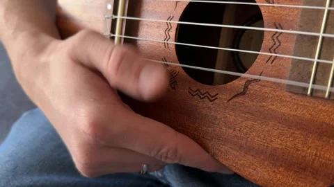 Man strumming ukulele strings close up at home, playing music, rhythm practice, Stock Footage 337104407