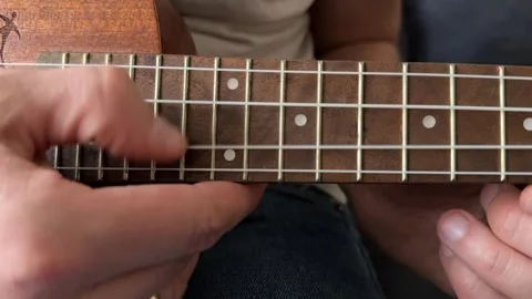 Man strumming ukulele strings close up at home, playing music, rhythm practice, Stock Footage 337104427