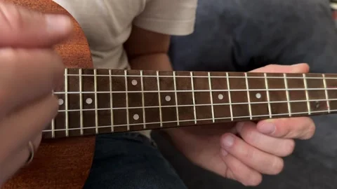 Man strumming ukulele strings close up at home, playing music, rhythm practice, Stock Footage 337104432