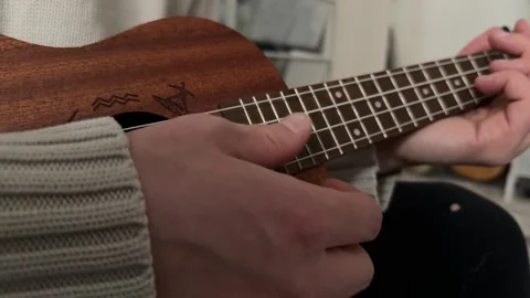 Man strumming ukulele strings close up at home, playing music, rhythm practice, Stock Footage 337105313