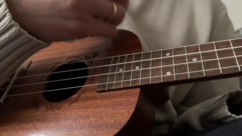 Man strumming ukulele strings close up at home, playing music, rhythm practice, Stock Footage 337105338