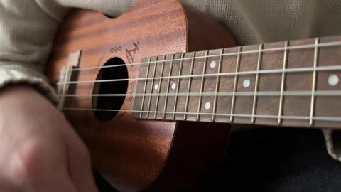 Man strumming ukulele strings close up at home, playing music, rhythm practice, Stock Footage 337105343
