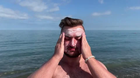 Man with stubble applies milk balm, lotion, sunscreen cream to face Stock Footage 332561053