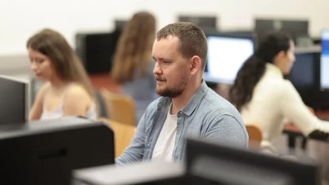 Man student of computer courses looks at monitor screen, types on keyboard and Stock Footage 310965921