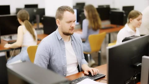 Man student of computer courses looks at monitor screen, types on keyboard and Stock Footage 311840421