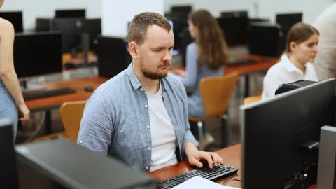 Man student of computer courses looks at monitor screen, types on keyboard and 스톡 동영상 330413109