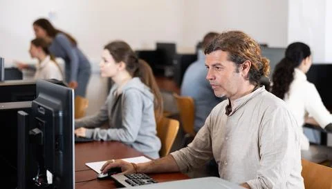 Man student of computer courses looks at monitor screen, types on keyboard and 스톡 사진