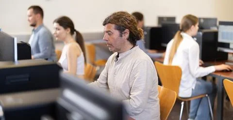 Man student of computer courses looks at monitor screen, types on keyboard and Stock Photos