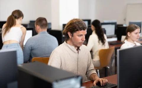 Man student of computer courses looks at monitor screen, types on keyboard and 写真素材