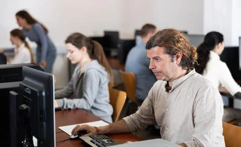 Man student of computer courses looks at monitor screen, types on keyboard and Stock Photos
