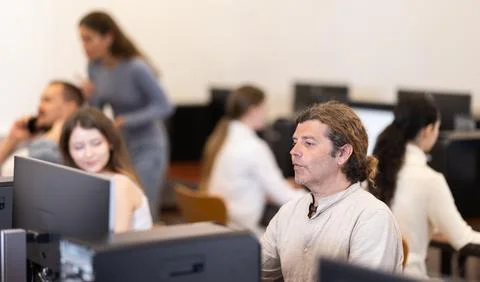 Man student of computer courses looks at monitor screen, types on keyboard and Stock-Fotos