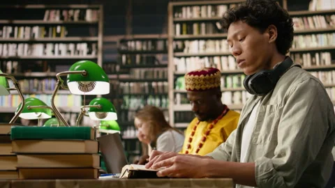 Man student with headphones reading notes from textbook at library table Stock Footage 337229157