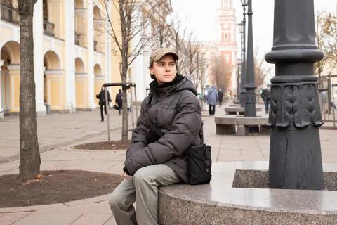 Man student sitting on stone bench in European city center and waiting. Cas.. Stock Photos