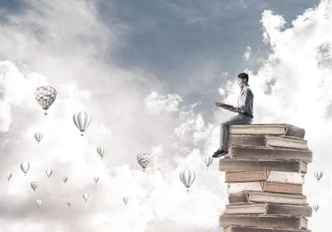 Man student on stack reading book and aerostats flying around Foto stock