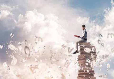 Man student on stack reading book and symbols flying around 库存照片