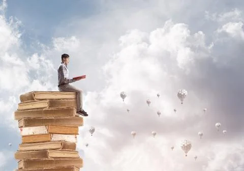Man student on stack reading book and aerostats flying around 库存照片