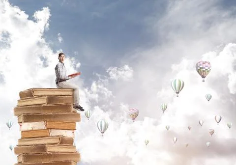Man student on stack reading book and aerostats flying around 库存照片