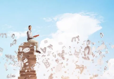 Man student on stack reading book and symbols flying around 库存照片