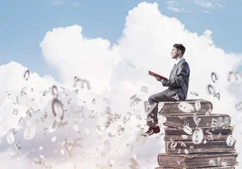 Man student on stack reading book and symbols flying around 库存照片