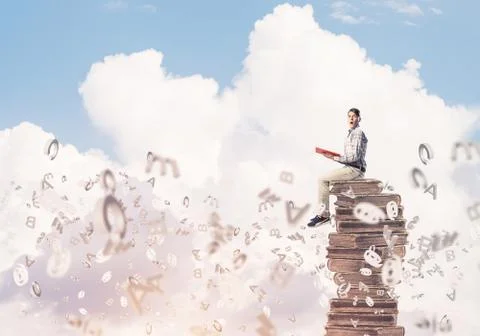Man student on stack reading book and symbols flying around 库存照片