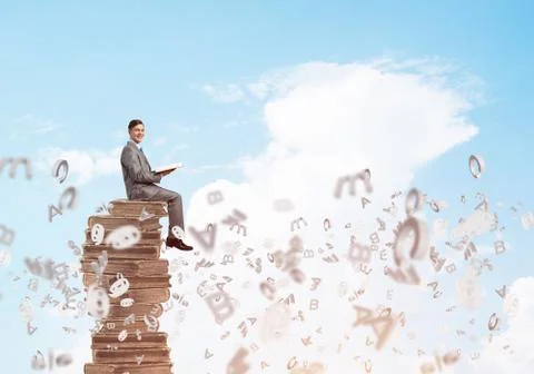 Man student on stack reading book and symbols flying around 스톡 사진