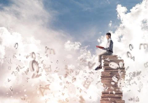 Man student on stack reading book and symbols flying around 스톡 사진