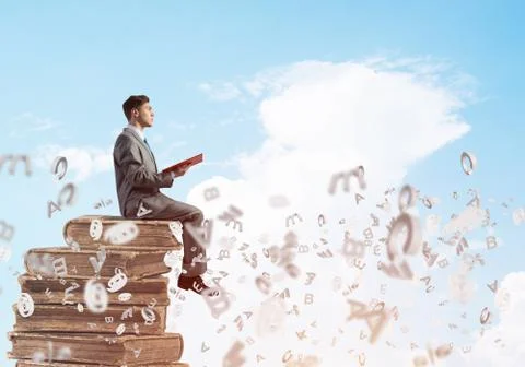 Man student on stack reading book and symbols flying around Foto stock