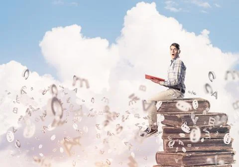 Man student on stack reading book and symbols flying around 库存照片