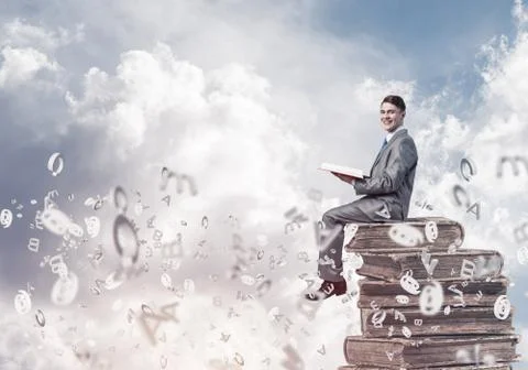 Man student on stack reading book and symbols flying around 库存照片