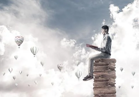 Man student on stack reading book and aerostats flying around 库存照片