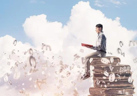 Man student on stack reading book and symbols flying around 库存照片