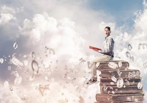 Man student on stack reading book and symbols flying around Foto stock