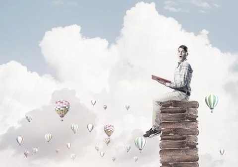 Man student on stack reading book and aerostats flying around Foto stock