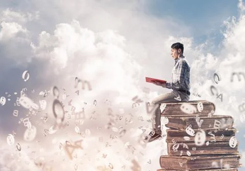 Man student on stack reading book and symbols flying around Foto stock