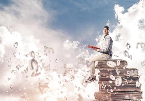 Man student on stack reading book and symbols flying around 库存照片
