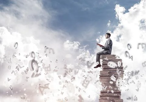 Man student on stack reading book and symbols flying around Foto stock