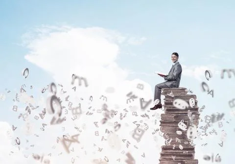 Man student on stack reading book and symbols flying around 스톡 사진