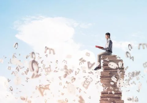 Man student on stack reading book and symbols flying around 库存照片