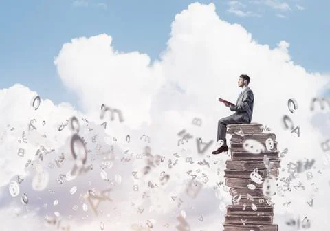 Man student on stack reading book and symbols flying around 库存照片