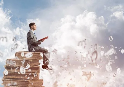 Man student on stack reading book and symbols flying around Foto stock