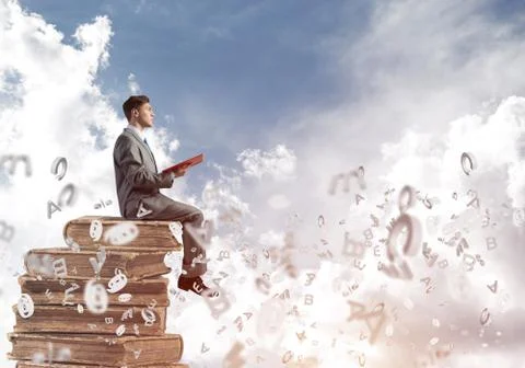 Man student on stack reading book and symbols flying around Foto stock