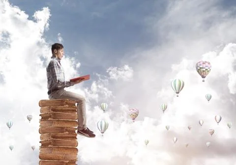 Man student on stack reading book and aerostats flying around 库存照片