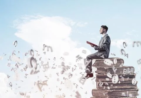 Man student on stack reading book and symbols flying around 库存照片