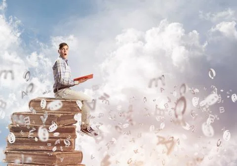 Man student on stack reading book and symbols flying around 库存照片