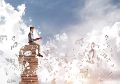 Man student on stack reading book and symbols flying around 库存照片