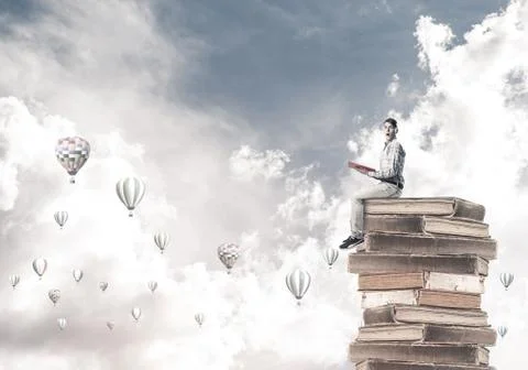 Man student on stack reading book and aerostats flying around 库存照片